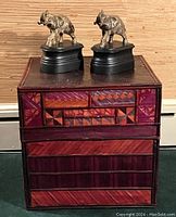 Pair of brass elephant statues on black carved wood plinths atop a woven reed storage box showing detailed geometric patterns on the box's front side.