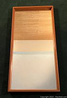 Full front view of the vertically hung rectangular mirror showing the teak frame and clear reflective glass.
