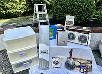 Photo displaying the stackable drawers, electric hotplate, cast iron crepe pan, garment rack box, cookbooks including Julia Child, and other kitchen items presented on a white surface outdoors.