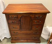 Frontal view of mahogany office chest showing 8 drawers and central Hobbit-like arched door with brass bail pull hardware