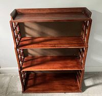 Front view of wooden vintage bookcase showing three shelves, flared top guard rails, and graduated shelf depth.