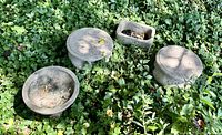 Overview of the four concrete garden items arranged on the ground among green foliage including birdbath, two mushroom stools, and a feeding trough.
