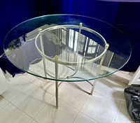 Full view of round glass table showing glass top and metal base with brass accents.