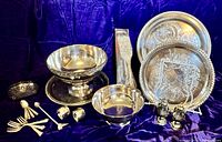 Wide view of entire silverplate collection showing trays, bowls, napkin rings, small forks and spoons, candle snuffer and napkin holder arranged on purple velvet.