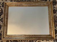 Full view of the rectangular gilded frame mirror on patterned carpet.