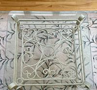 Top-down view of square glass coffee table showing ornate cast iron scroll base and glass top.