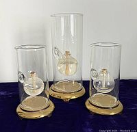 Three assembled oil lamps—two 6"H and one 9"H—on fabric background