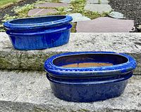 Two cobalt blue oval ceramic planters side by side on stone steps showing overall shape and glaze