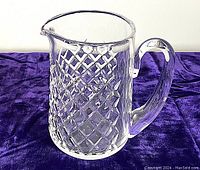 Clear Waterford Alana crystal pitcher with diamond cut pattern shot from a side angle highlighting handle and spout on purple fabric background.