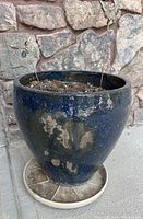 Photo of a single large blue ceramic planter showing wear and sitting on saucer with soil and decorative garden stakes.