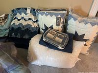 Crochet blanket alongside several bedding items including pillows and quilted star-patterned sets in plastic packaging.