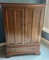 Front view of Drexel wood cabinet with closed two doors and drawer. Shows medium brown finish, recessed panels on doors, and brass hardware.