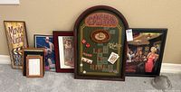 Photo showing entire lot grouped on floor next to wall, 7 pieces visible including movie night sign, casino art, Coca Cola and lounge scene art, plus smaller frames