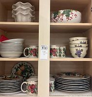 Photo of shelves showing multiple plates, bowls, and mugs with fruit and floral patterns arranged in groups.
