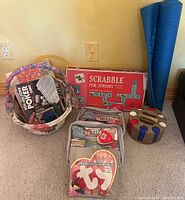 Lot overview showing basket with Poker Bingo and card games, Scrabble for Juniors red board game box, vintage Ty 1999 calendar, and poker chip holder with chips.