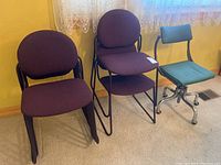 Three purple fabric stacking chairs with black metal frames and one green fabric rolling office chair on beige carpet, near a wall with yellow paint and sheer curtains.