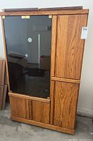 Full front view of wooden stereo cabinet with black glass front door and wood paneled side compartments.
