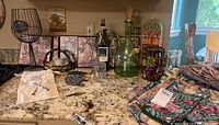 Wide view of the counter showing a string light wine bottle lamp, wall art, wine cork holders, decorative glassware, and several folded table linens