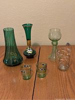 Photo showing the full set of 6 green glass items including two vases, three glasses, and two small hand decorated glasses.