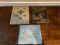 Photo of three antique children's picture books on a wooden table, titles visible include "Footsteps of Jesus" and "The One Shoe Story Book". The third book shows an ornate floral pattern on the cover.