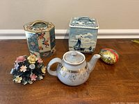 Full lot showing all ceramic tea tins, teapot and flower sculpture on wood surface.