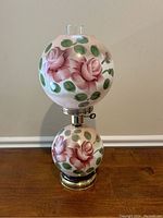 Front view of early American style hand painted double globe electric lamp with rose motif on white glass globes, metal base, and hurricane glass shades.