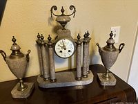 Full view of antique marble clock and two matching garniture finials on wooden surface.