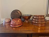 Wide view of set showing copper jello molds, copper sieve/colander with steel interior, and three nesting copper oval bowls with brass handles