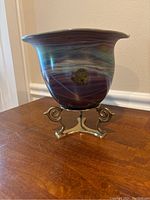 Side and front view of the hand blown glass bowl with purple and blue swirling patterns sitting on an ornate brass stand.