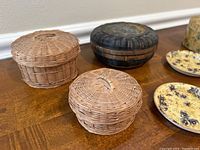 Three small antique woven baskets in various sizes and colors on a wooden surface.