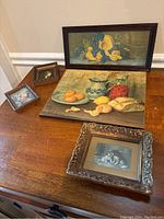 Overall view of four framed antique prints on wooden surface, including still life and dog portraits