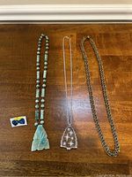 Photo shows three necklaces laid out flat on wood surface and a small card with mother of pearl earrings shaped as bows.