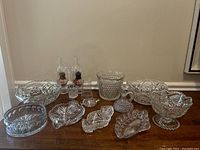 Photo showing the full spread of vintage pressed glass items laid out on table including fairy lamps, ice bucket, serving dishes, and small bowls.