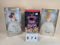 Three boxed Barbie dolls displayed with a notepad showing lot number; includes two Wedding Day Barbie reproductions in white gowns and one Mardi Gras Barbie in a purple costume.