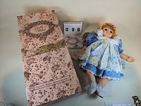 Photo of doll lying next to original box and reference card showing collection number 098, showcasing doll outfit and condition.