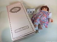 Photo of the 17-inch Terri doll dressed in floral dress alongside its original box labeled Dolls by Pauline with designer name.