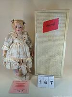Porcelain Elite Doll in Victorian-style dress standing next to original box and certificate of authenticity.
