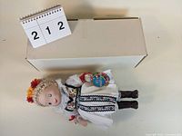 Full view of the musical doll lying next to the box, showing the doll in costume with braided hair and flowers.