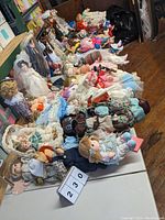 Photo showing a large collection of unboxed dolls placed on tables, showcasing a wide range of styles, outfits, and sizes.