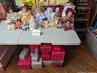Wide shot showing collection of approximately 14 dolls arranged on a table, along with their assorted boxes placed underneath and beside the table.