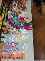 Photo showing a large assortment of Ty Beanie Baby plush toys spread out on a table with visible hang tags and various colors and designs.
