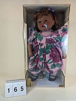 22 inch Lissi limited edition doll named Yvonne displayed in original box wearing floral pink dress with purple and green highlights, white socks, and black shoes.
