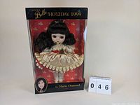 Marie Osmond Adora Belle 1999 Holiday Doll in original box with packaging and display background featuring holly leaves, showing full doll and box front.