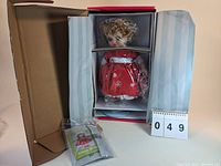 Full view of the doll inside original packaging with protective plastic covering on the head, and included packaging materials visible.