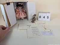 Photo showing the Marie Osmond Baby Marie doll inside original box, certificate, necklace, and bear figurine on table.