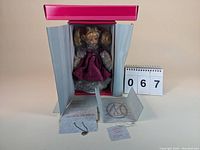 Front view of the Marie Osmond Helena Tiny Tots doll in original box with certificate and necklace displayed.