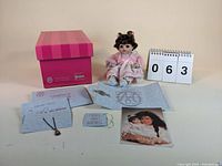 Photo showing the doll seated with the pink box, a certificate of authenticity, tags, and a photo of Marie Osmond with the doll.