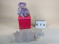 Full view of the Sabrina Fairy Tot doll seated on a pink box with accompanying packaging materials and accessories laid out in front.