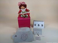 Marie Osmond collectible doll seated on pink box with certificate and paperwork laid out.