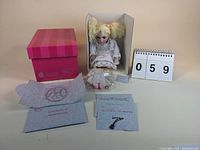 Full lot photo showing seated Marie Osmond collectible doll in original holder, certificate of authenticity, necklace on card, and pink presentation box.